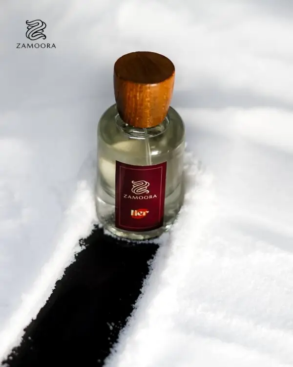 Zamoora HER perfume bottle for women placed among pink flowers with a purple background, highlighting fruity top notes of strawberry, raspberry, blackberry, sour cherry, black currant, mandarin orange and lemon, a heart note of violet jasmine, and base notes of musk, vanilla, cashmeran, woody notes, amber, oakmoss and patchoulI.